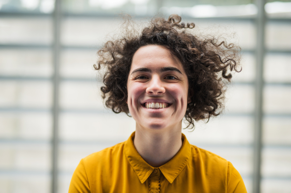 A portrait of a young student or businesswoman standing indoors in room in a library or office.