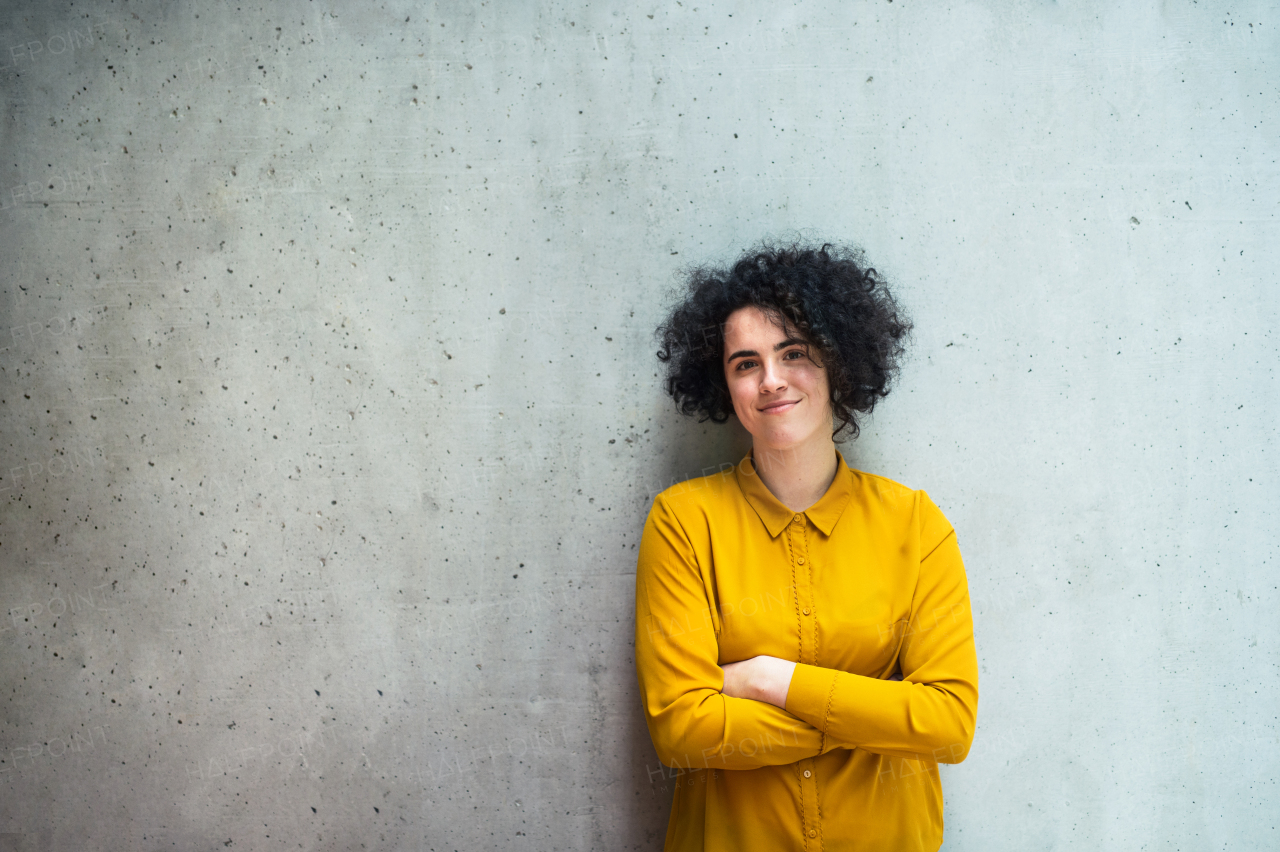 A portrait of a young student or businesswoman standing in room in a library or office, arms crossed.