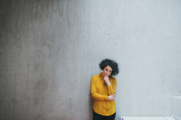 A portrait of a sad student or businesswoman standing in room in a library or office.