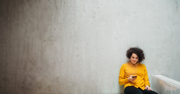 Portrait of a young student or businesswoman with smartphone sitting on desk in room in a library or office. Copy space.