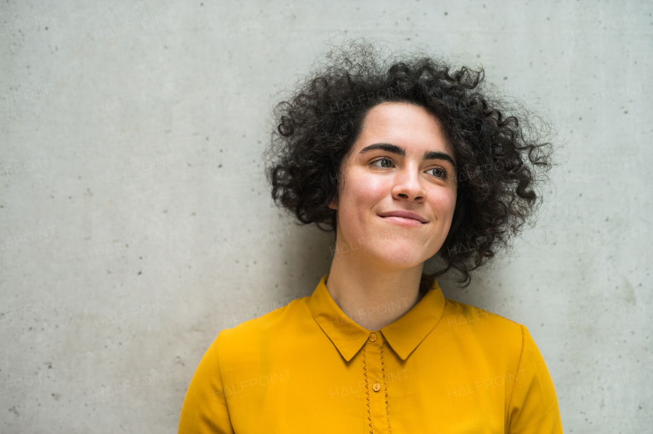 Portrait of a young student or businesswoman standing against gray concrete background.