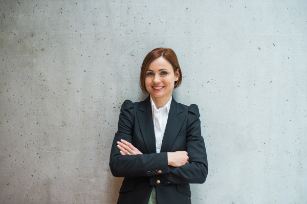 A portrait of young cheerful businesswoman standing in office, looking at camera.