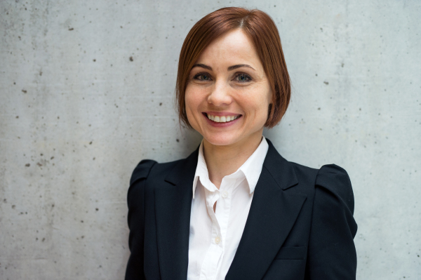 A portrait of young cheerful businesswoman standing in office, looking at camera.