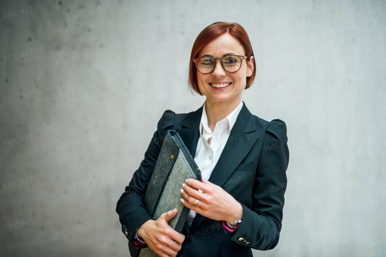 A portrait of young cheerful businesswoman standing in office, looking at camera.