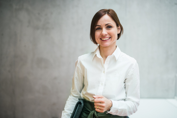 A portrait of young cheerful businesswoman standing in office, looking at camera.