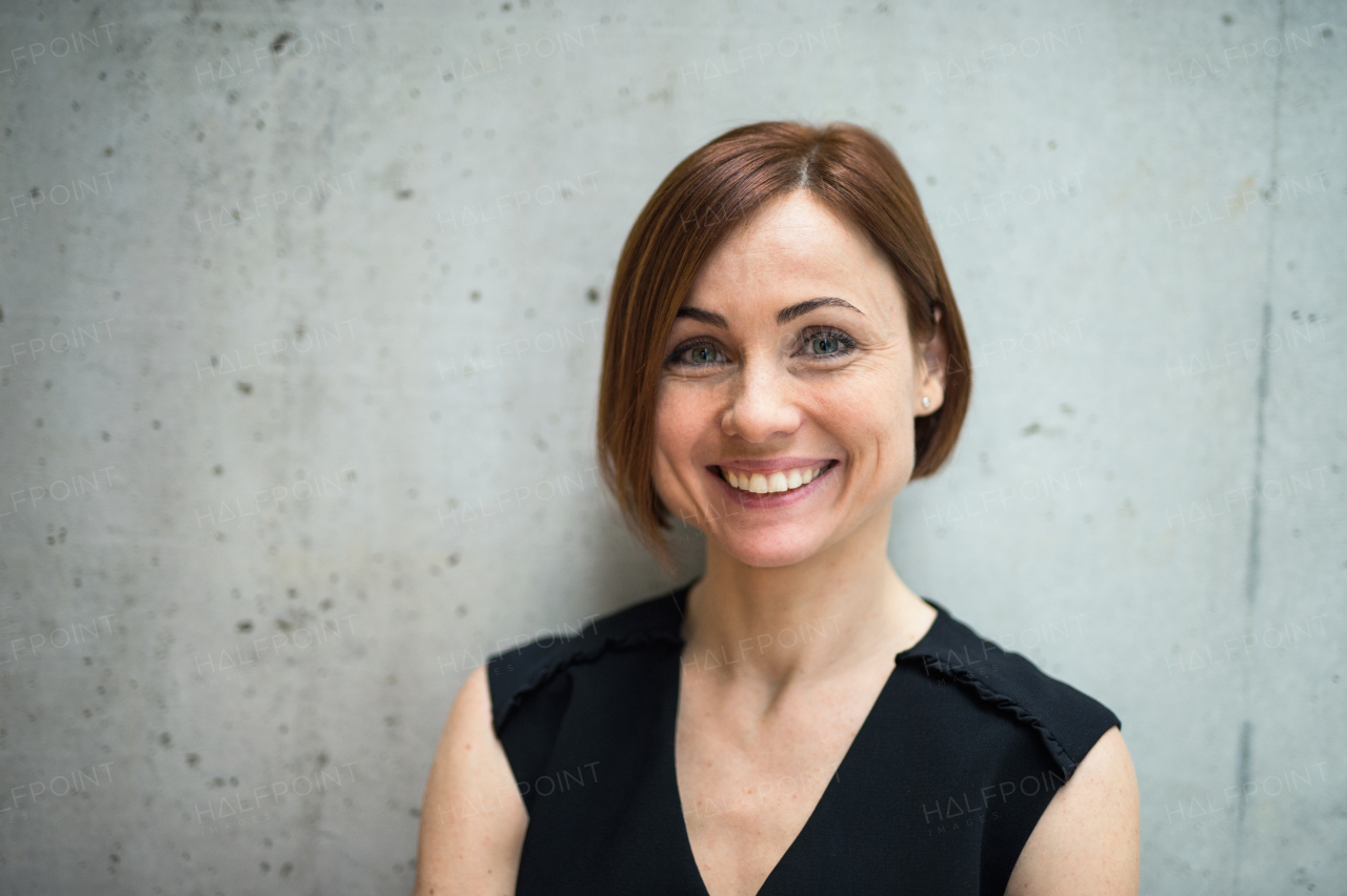 A portrait of young cheerful businesswoman standing in office, looking at camera.