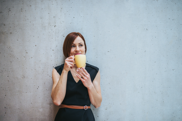 A portrait of young cheerful businesswoman standing in office, holding a cup of coffee.