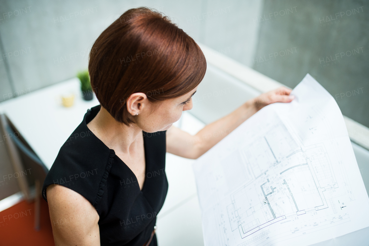 A young businesswoman or architect standing in office, looking at blueprints.