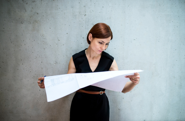 A young businesswoman or architect standing in office, looking at blueprints.