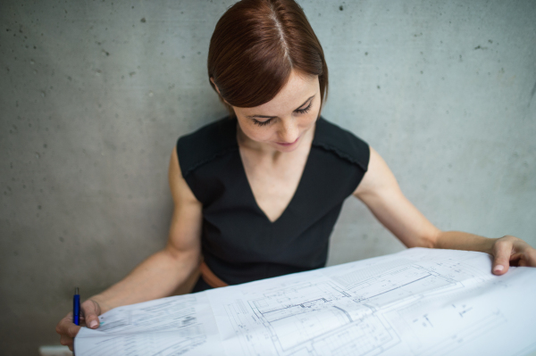 A young businesswoman or architect standing in office, looking at blueprints.