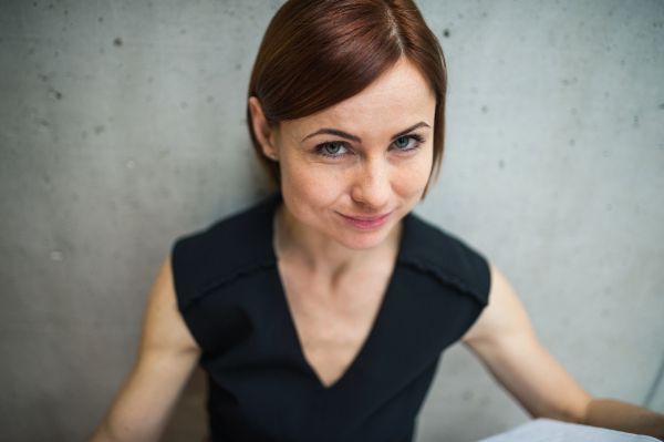 A portrait of young cheerful businesswoman standing in office, looking at camera.