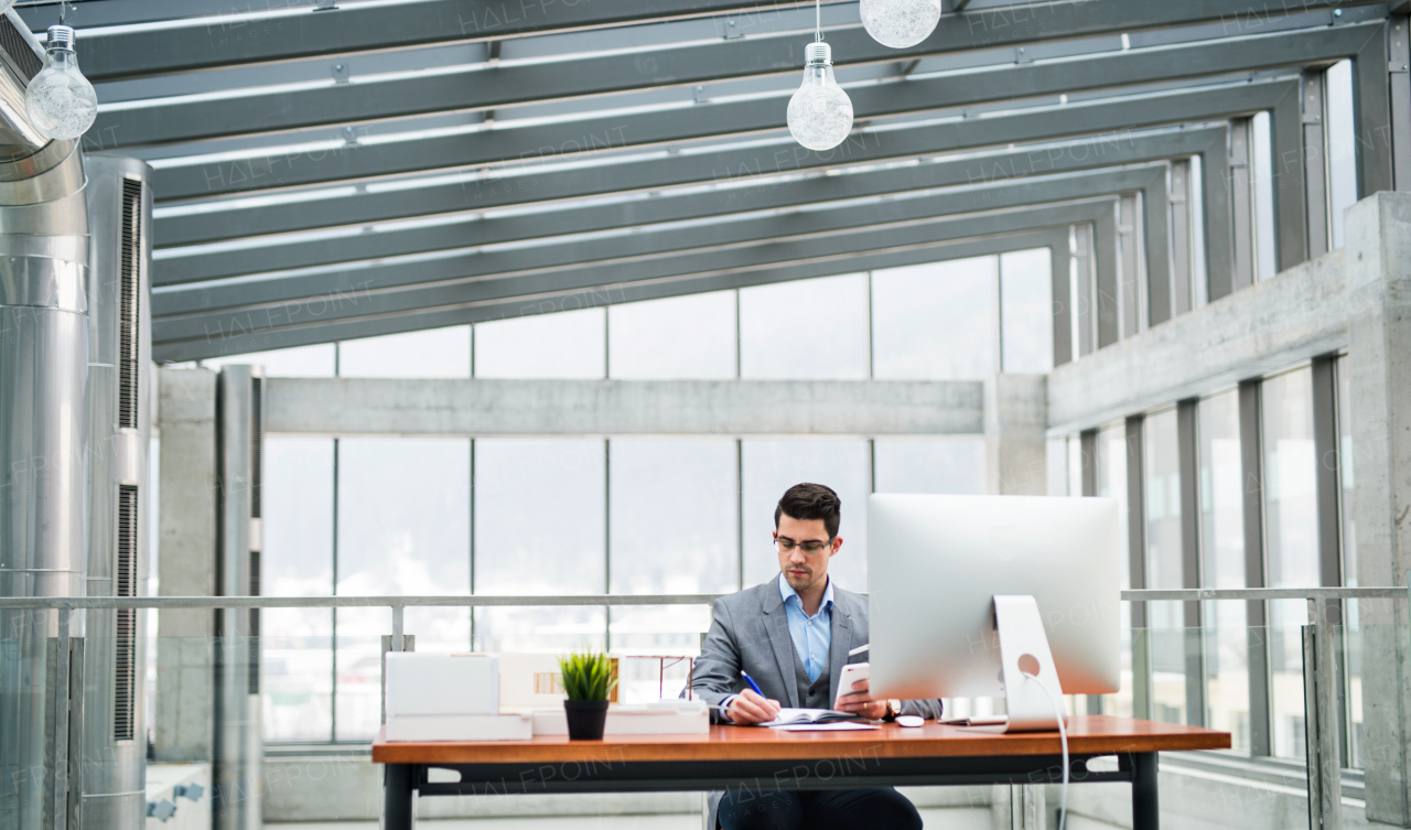 Young businessman or architect with model of a house standing at the desk in office, working.