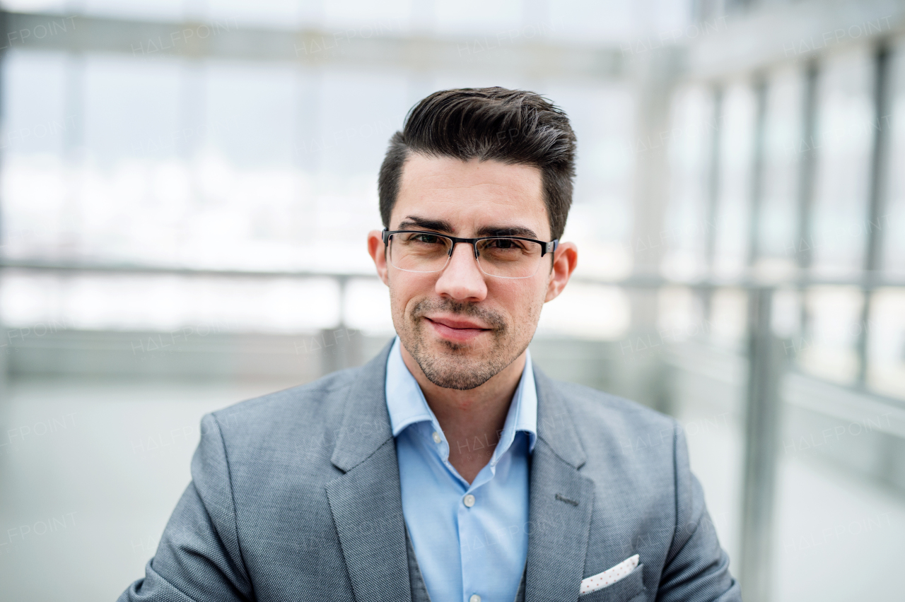 A front vire of portrait of young businessman indoors in an office. A close-up.