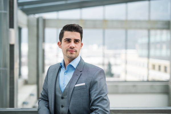 A portrait of young content businessman standing in corridor outside office. Copy space.