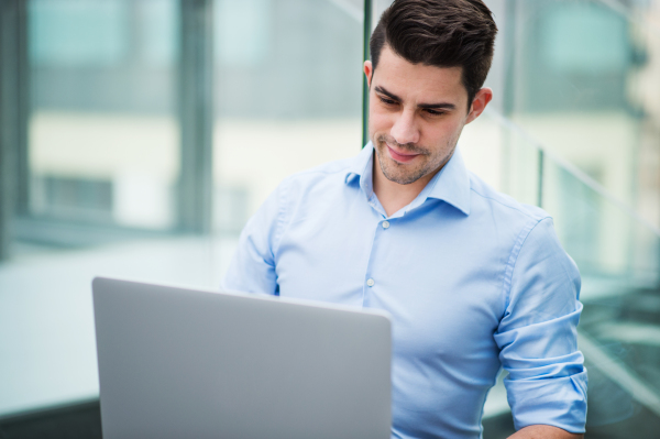 A portrait of young handsome businessman with laptop sitting in office.