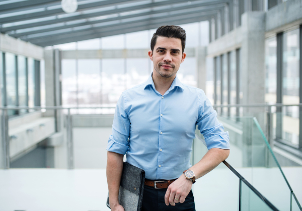 A young businessman standing in corridor outside office, looking at camera.