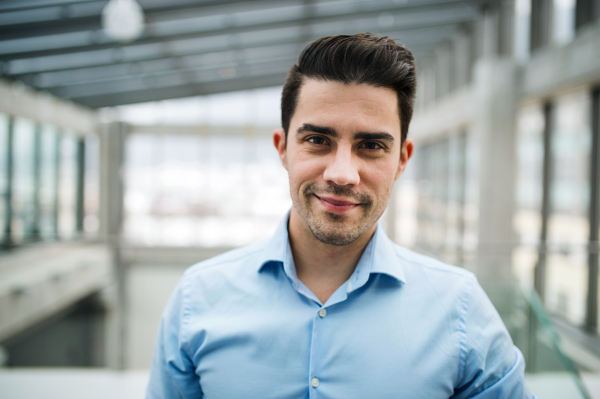 A portrait of young businessman standing indoors in an office. Copy space.