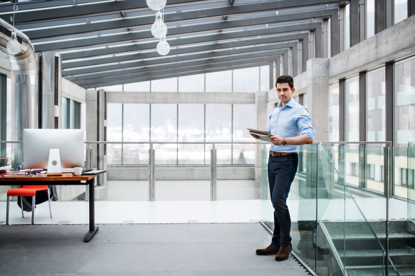 A portrait of young businessman standing indoors in an office, looking at camera. Copy space.