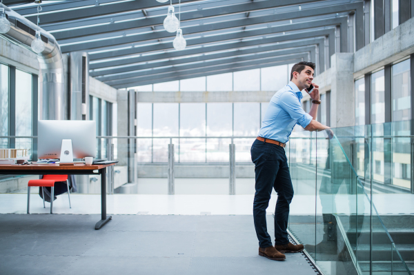 A side view of young businessman with smartphone in an office, making a phone call. Copy space.