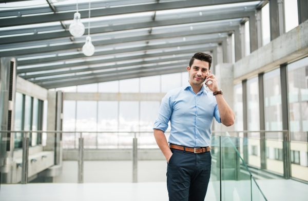 A side view of young businessman with smartphone in an office, making a phone call. Copy space.