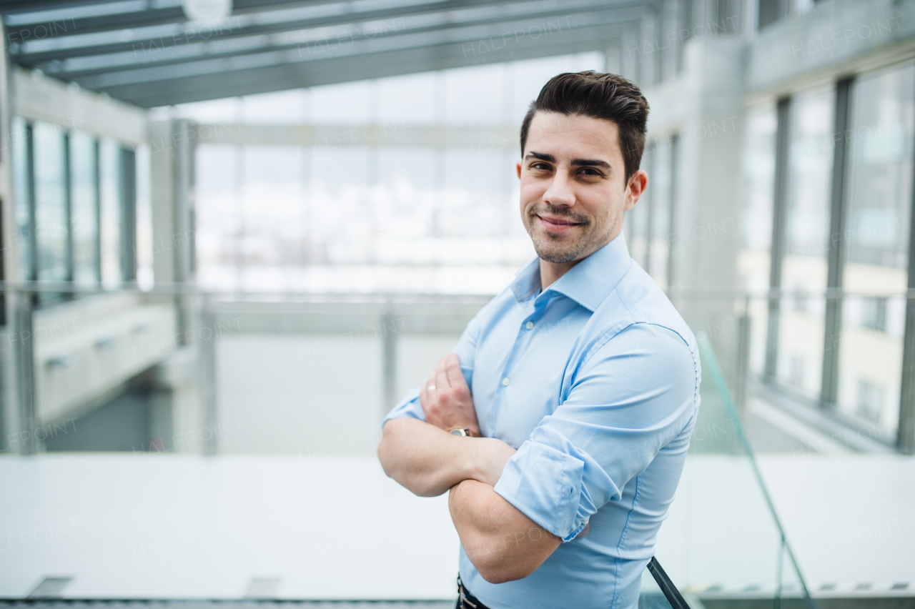 A portrait of young businessman standing indoors in an office, arms crossed. Copy space.