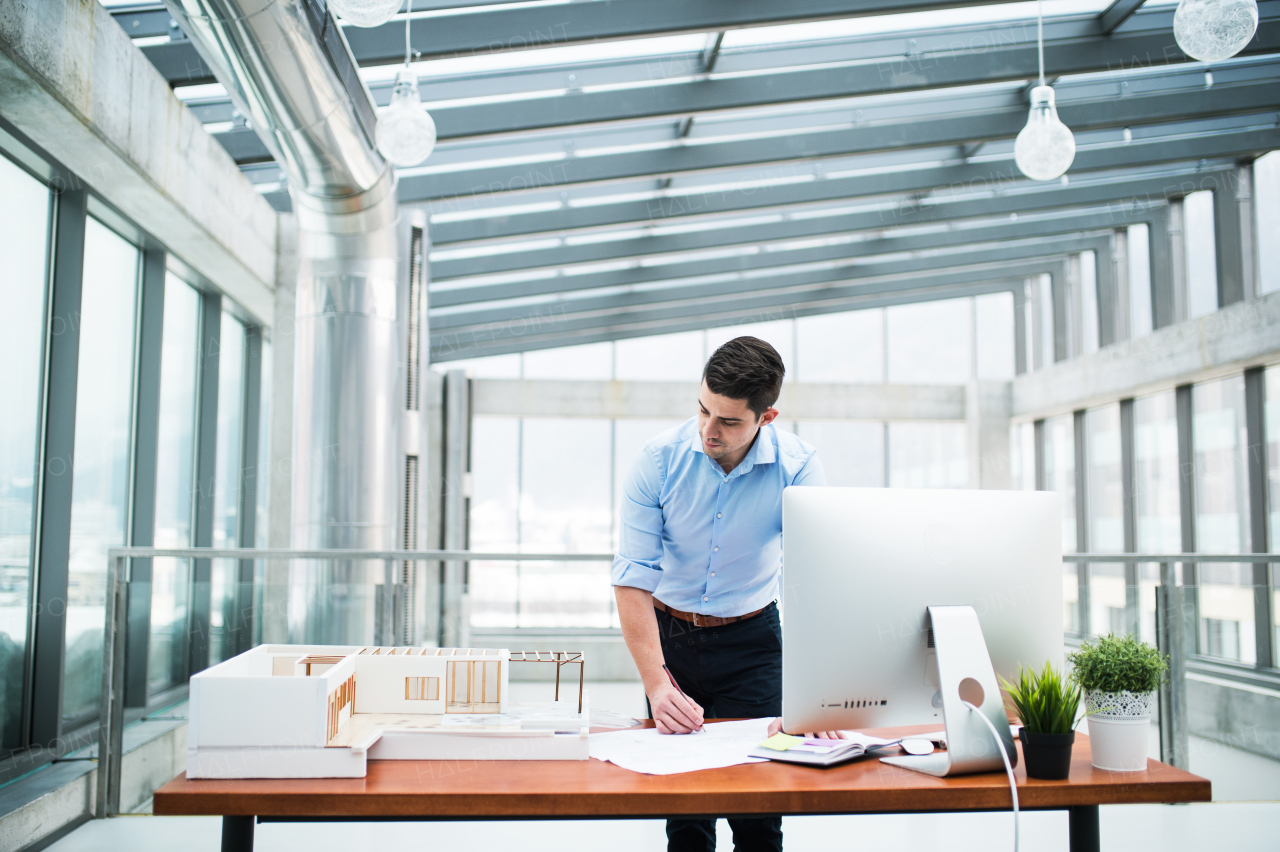 Young businessman or architect with model of a house standing at the desk in office, working.