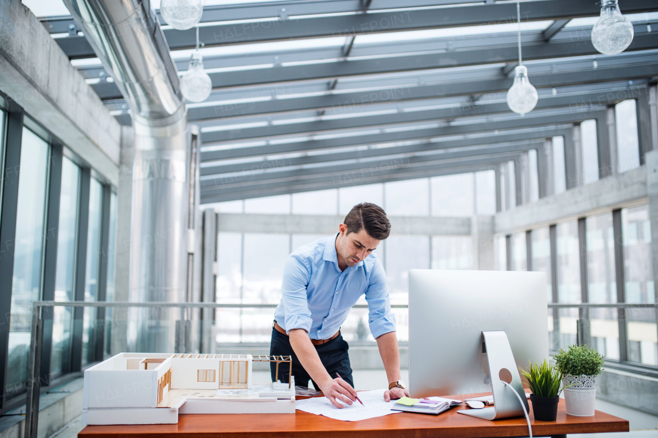 Young businessman or architect with model of a house standing at the desk in office, working.