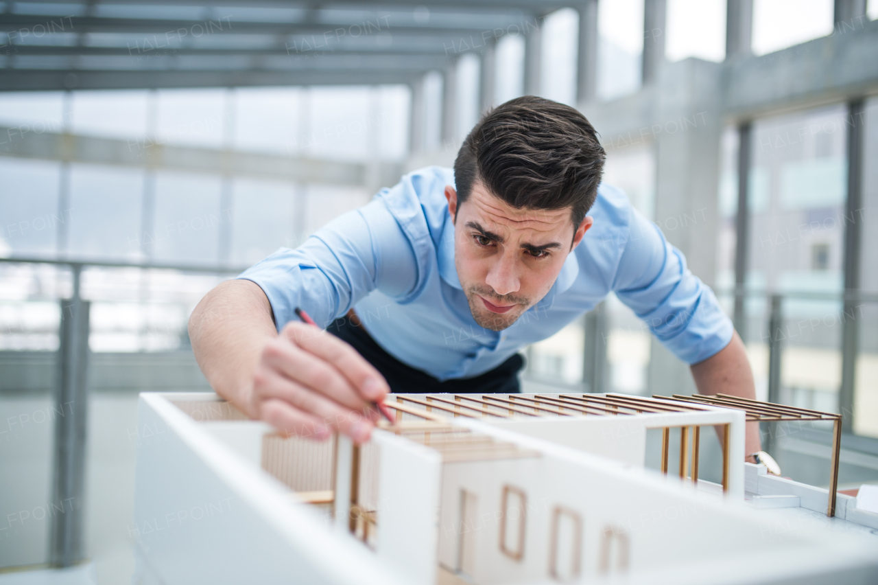 Young businessman or architect with model of a house standing at the desk in office, working.