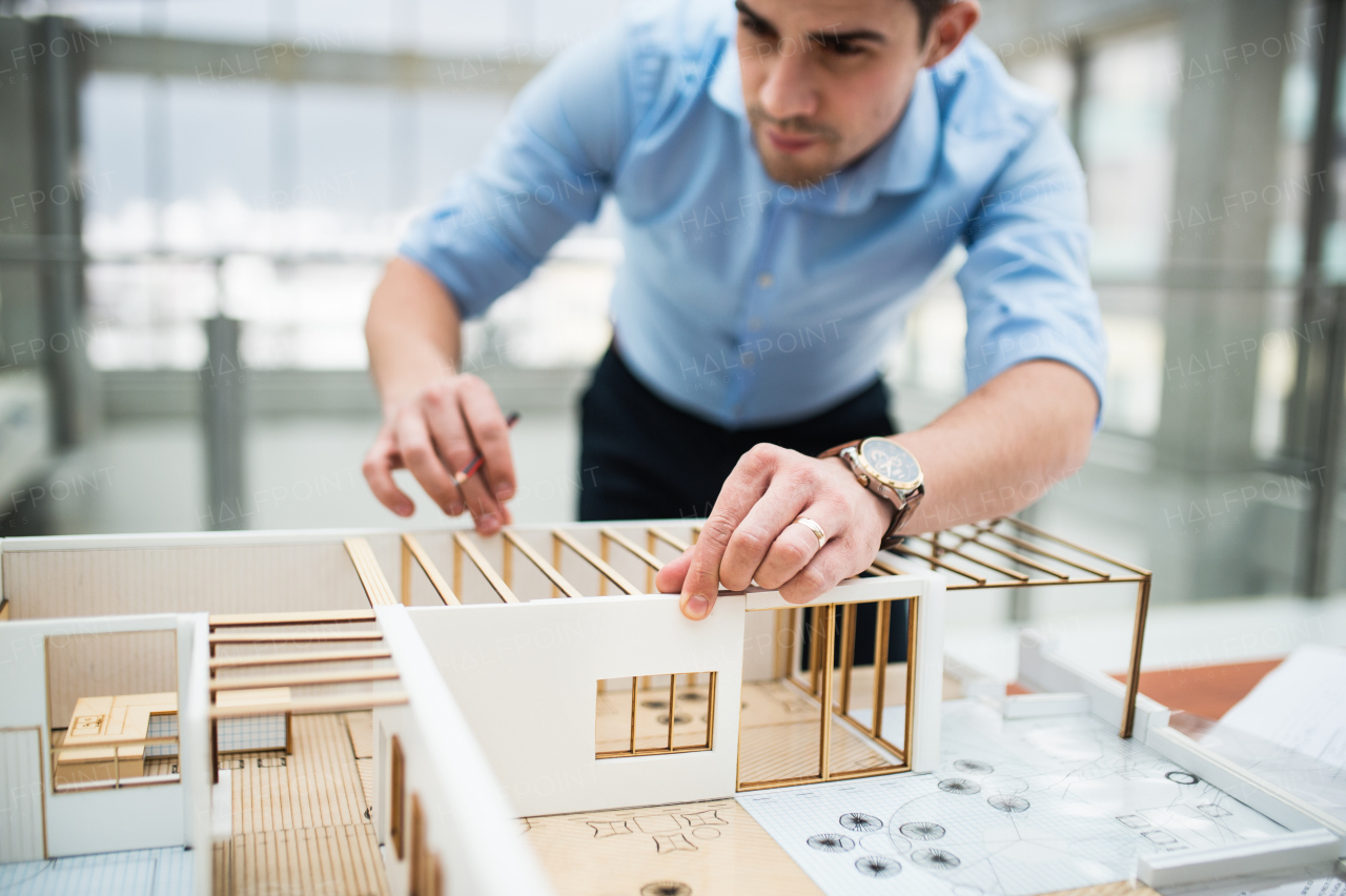 Young businessman or architect with model of a house standing at the desk in office, working.