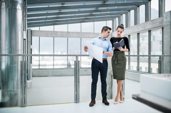 Two young male and female architects with blueprints standing in office, talking.