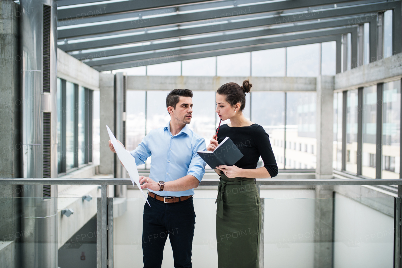 Two young male and female architects with blueprints standing in office, talking.