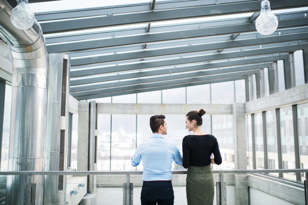 A rear view of young businesspeople standing in office, talking.