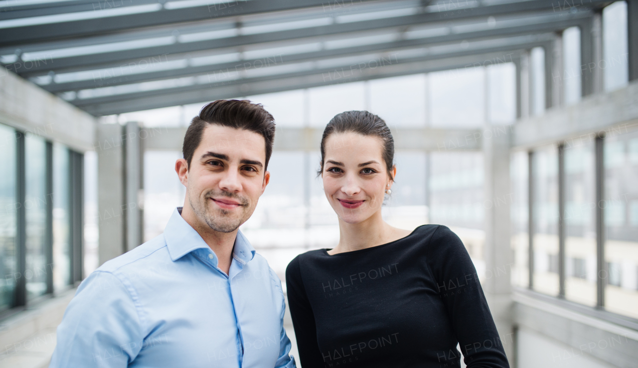 Two young male and female architects standing in office, looking at camera.