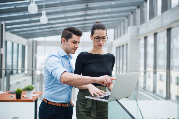 Two young male and female architects or businesspeople with laptop standing in office, talking.