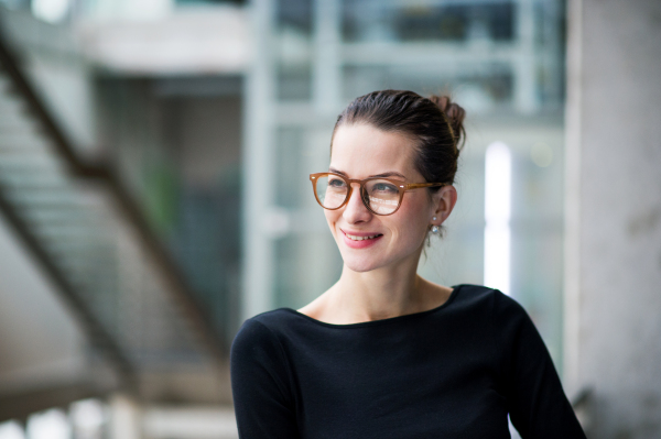 A waist-up portrait of young businesswoman standing in corridor outside office.