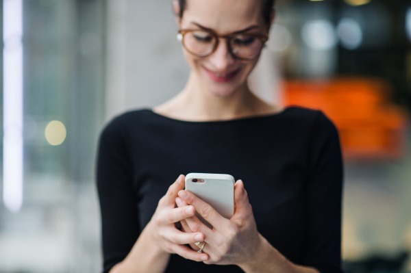 A young business woman with smartphone and glasses against in office.