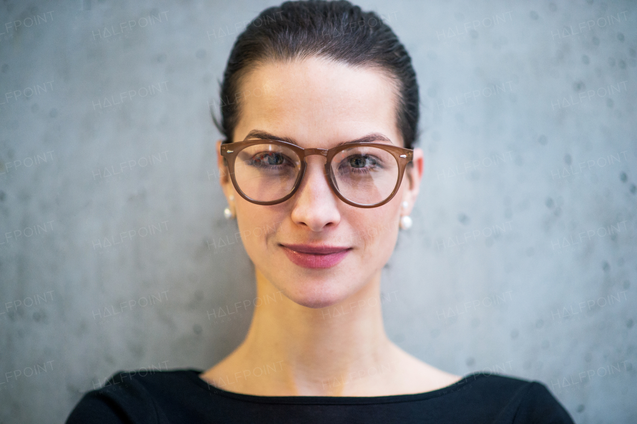 A portrait of young businesswoman with glasses standing in office, looking at camera.