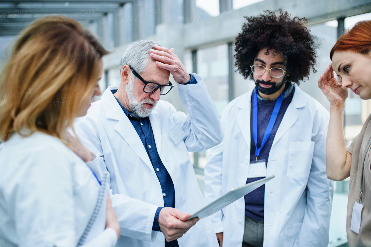 A group of worried doctors with tablet on conference, medical team discussing issues.