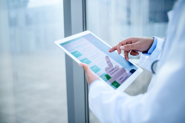 Midsection of unrecognizable doctor with tablet standing in hospital, working.