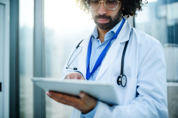 Portrait of worried male doctor with tablet standing in hospital. Copy space.