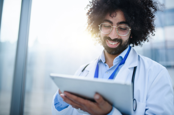 Portrait of cheerful male doctor with tablet standing in hospital. Copy space.