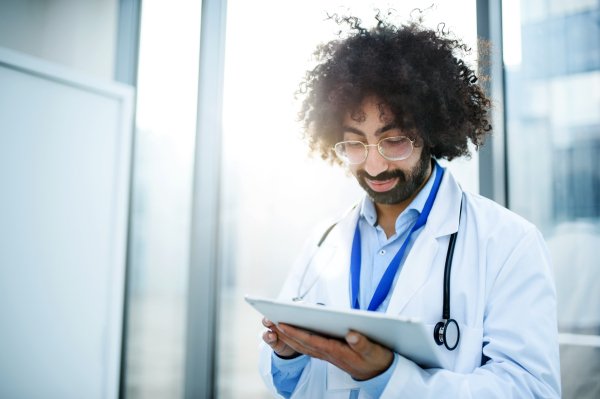 Portrait of male doctor standing in hospital, using tablet. Copy space.