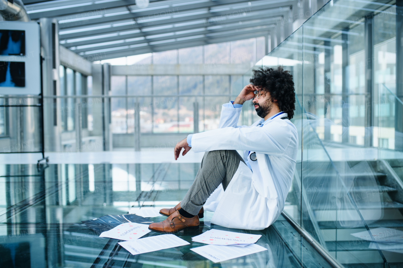 Side view of worried and tired doctor sitting on floor in hospital, corona virus concept.