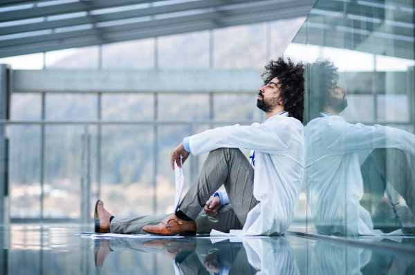 Serious and frustrated man doctor sitting on the floor, corona virus concept.