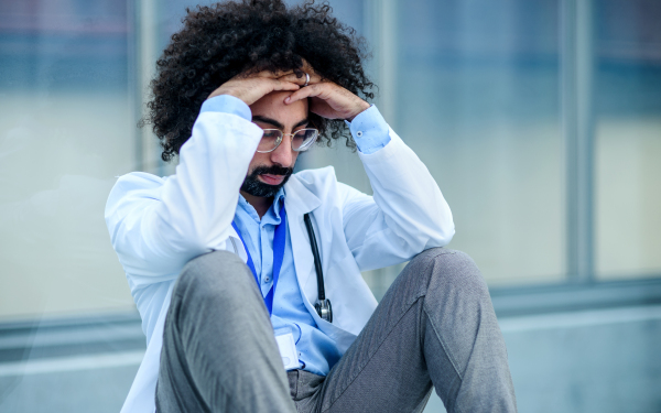 Worried and tired mixed raced doctor sitting on floor in hospital, corona virus concept.