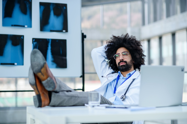 Portrait of male doctor with and feet on desk at X-ray in hospital, corona virus concept.