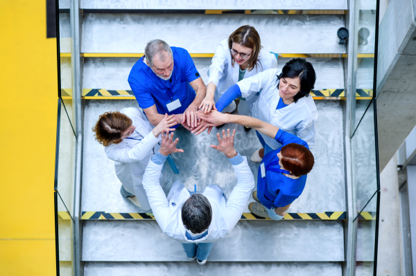 Top view of group of doctors standing on stairs on conference, putting hands together.