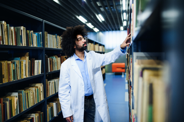 Doctor standing in library, looking for a book on shelf. Study and research concept.