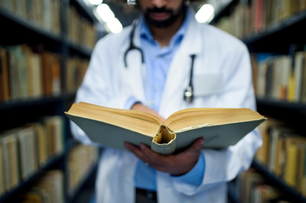 Unrecognizable doctor with book in library, studying information about corona virus.