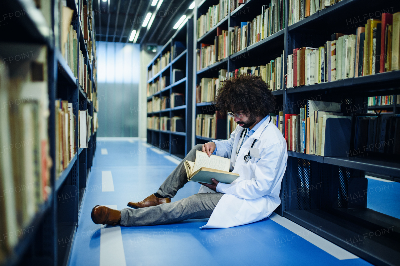 Portrait of male doctor sitting in library, studying information about corona virus.